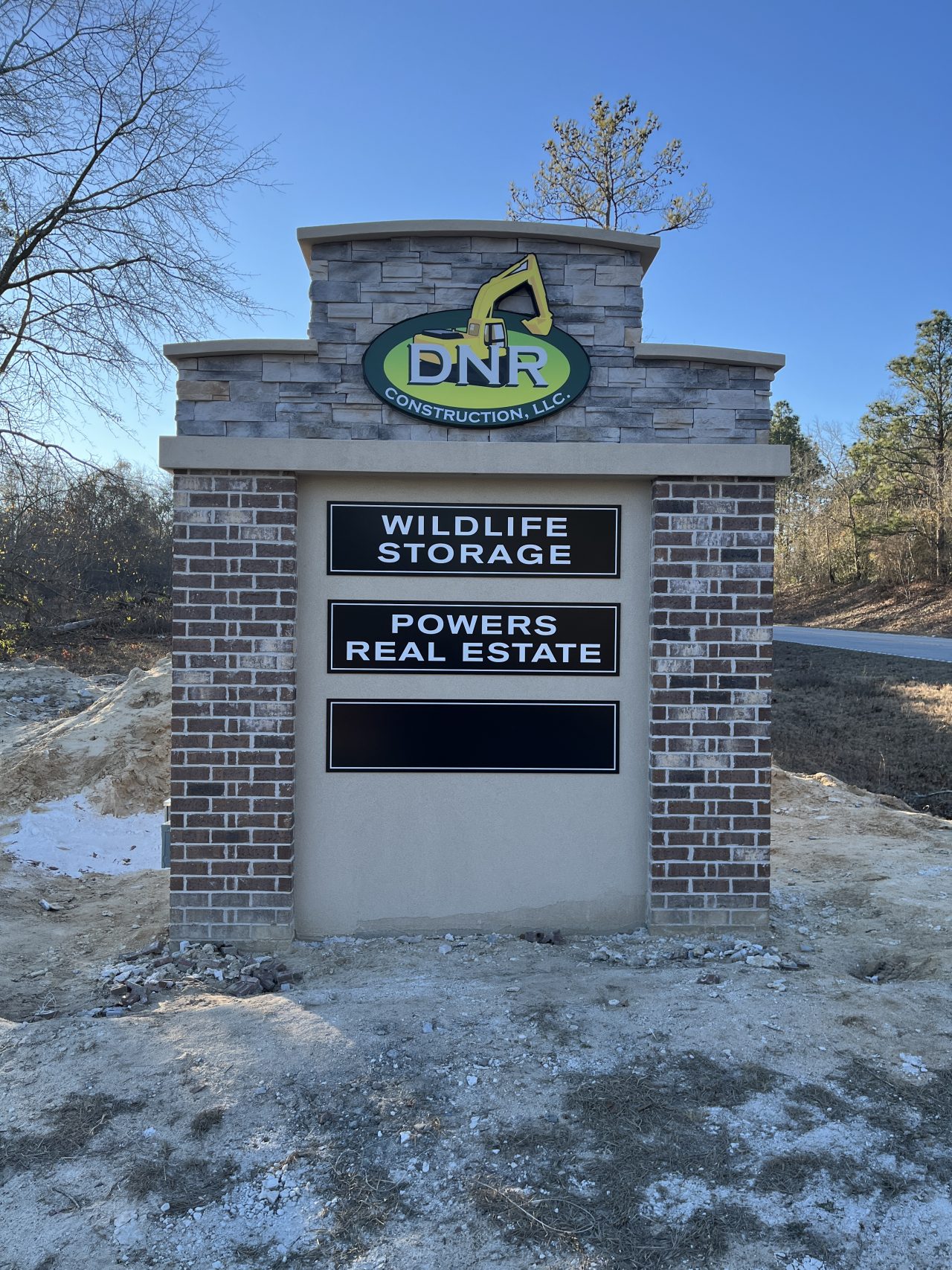 Brick monument sign with illuminated logo at the top and three black panel signs underneath.